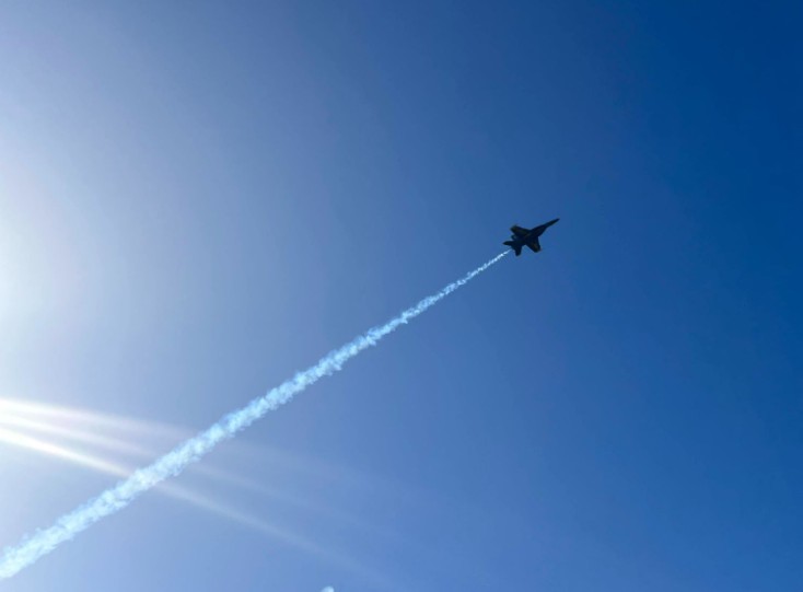 A Blue Angels jet with a vapour trail against a blue sky